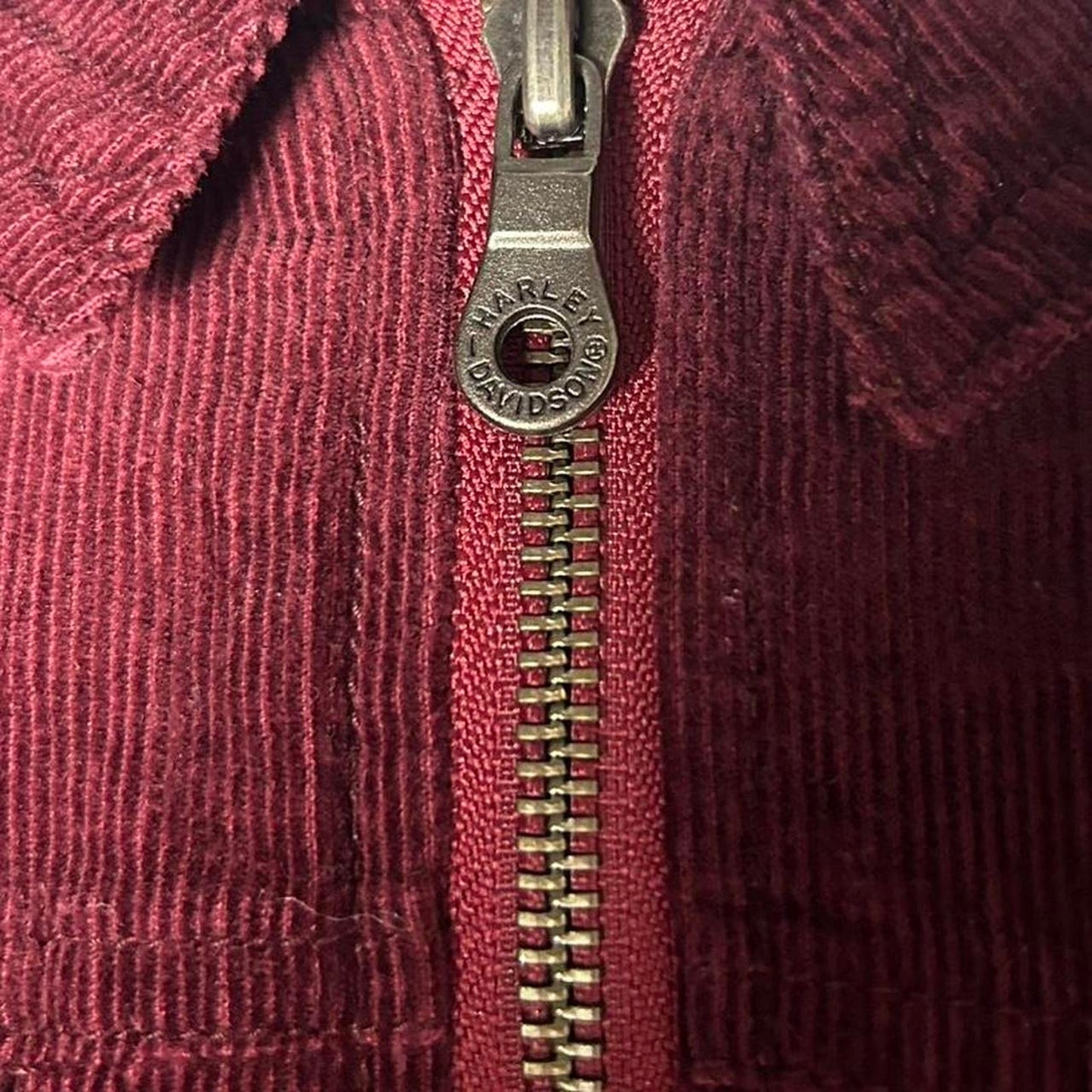 Close-up of a red corduroy jacket with a zipper and Harley-Davidson logo.